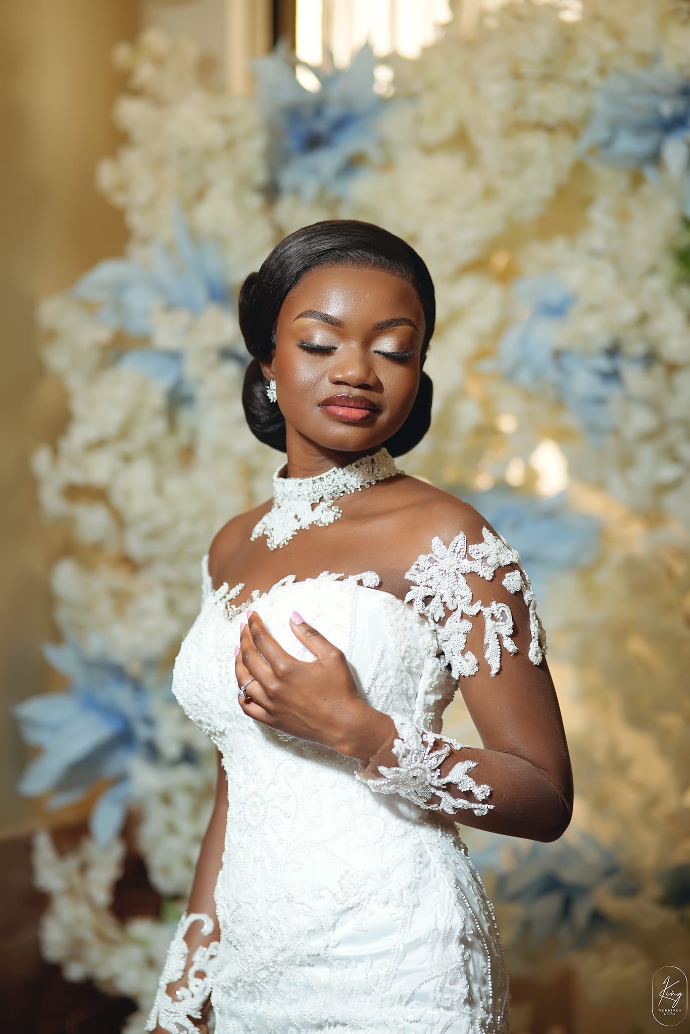 Eyes-closed bridal portrait with lace collar and floral bokeh