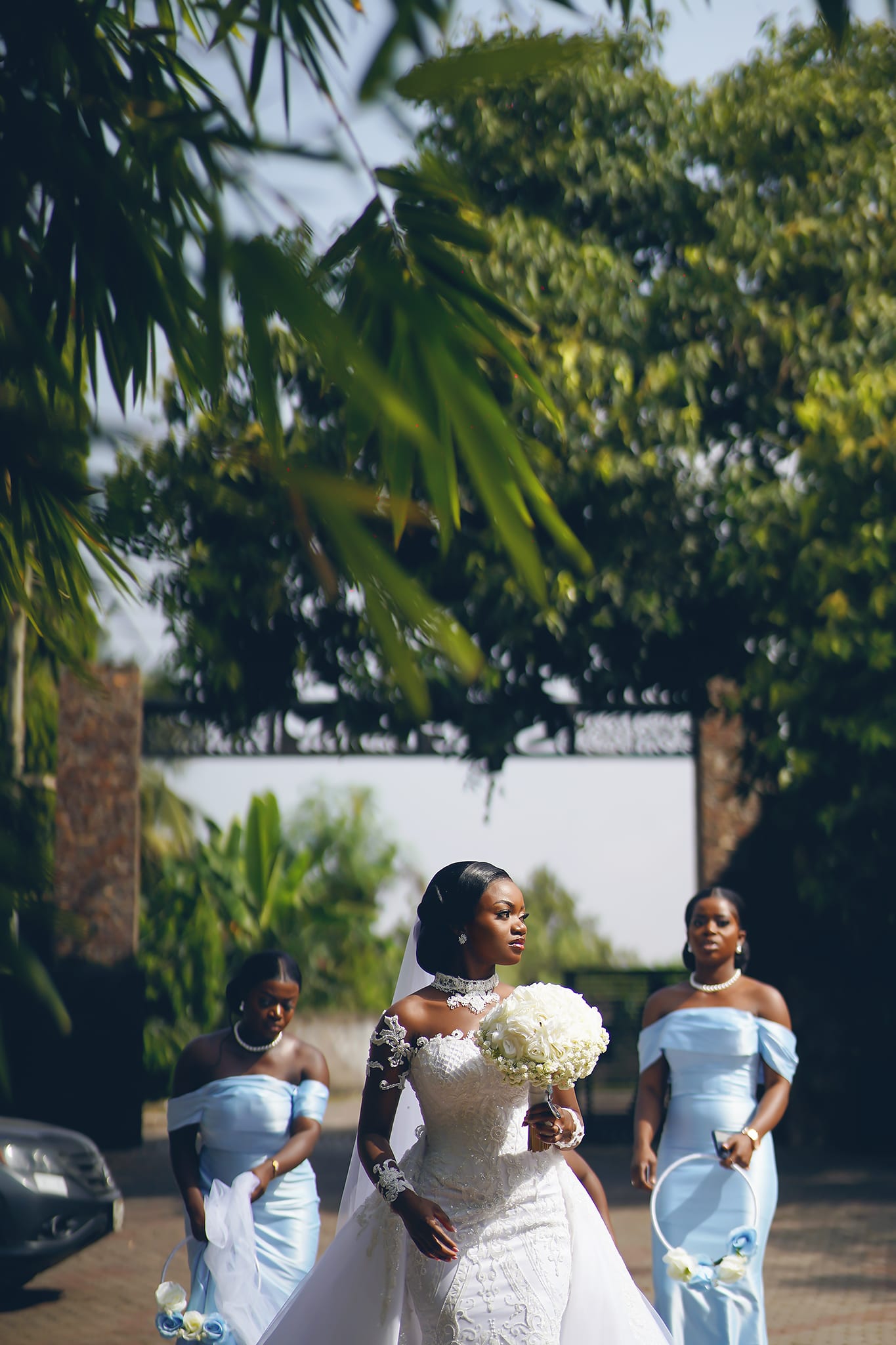 Bride with bridesmaids in soft blue walking through green foliage