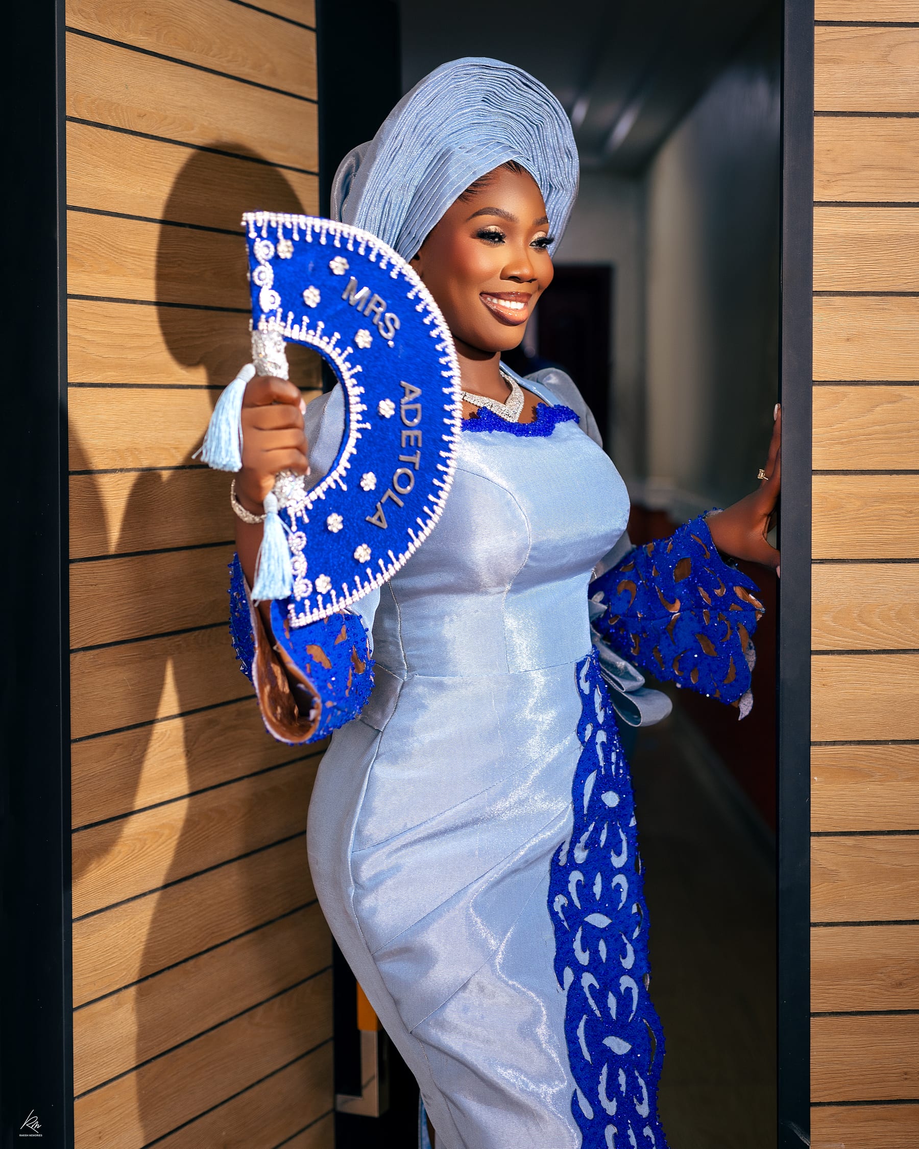 Bride in blue gele and lace gown holding a personalized fan