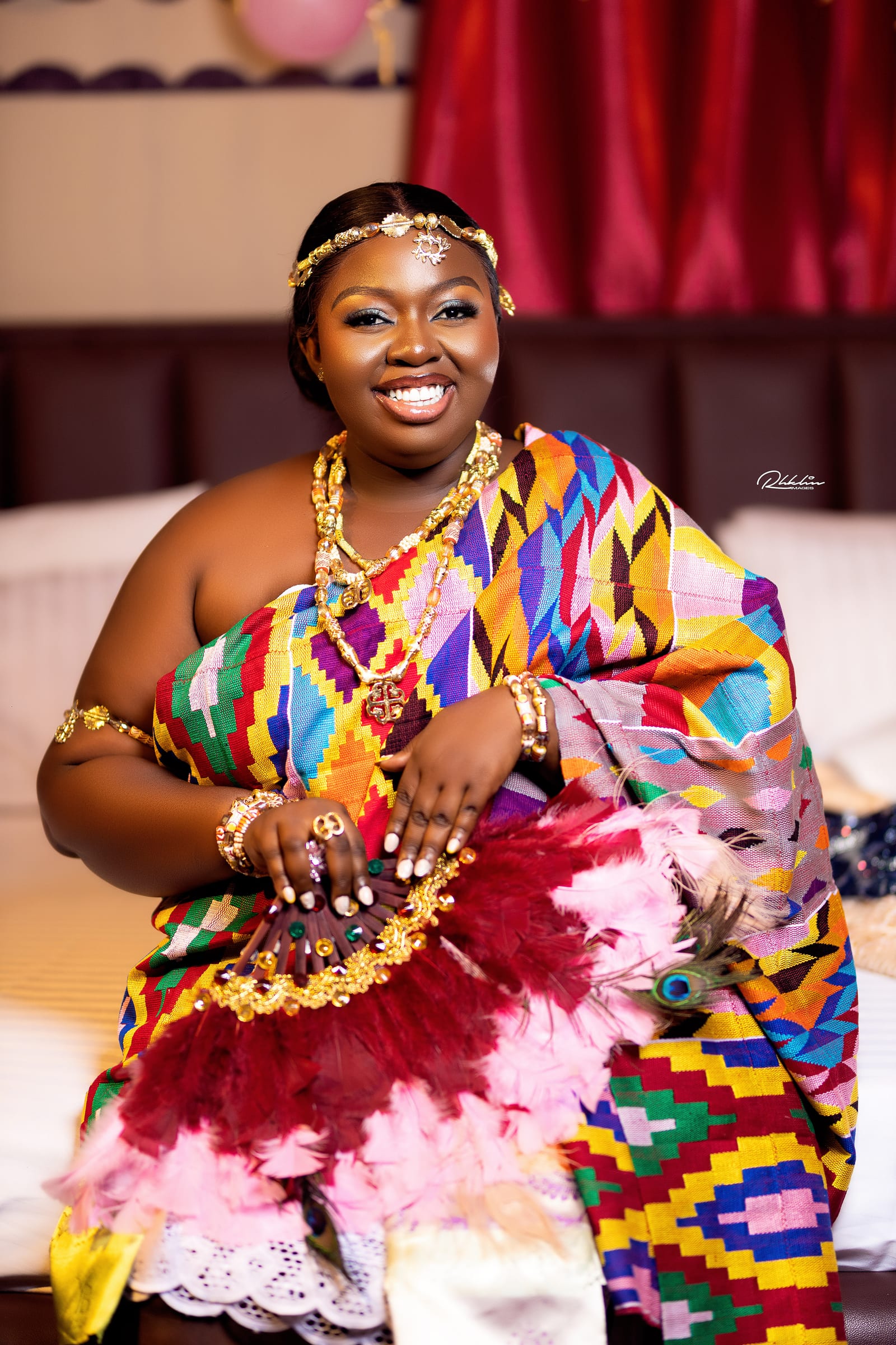 Traditional bride in kente with layered gold and a feather fan